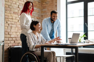 Multiracial smiling three colleagues talking and working with laptop in office